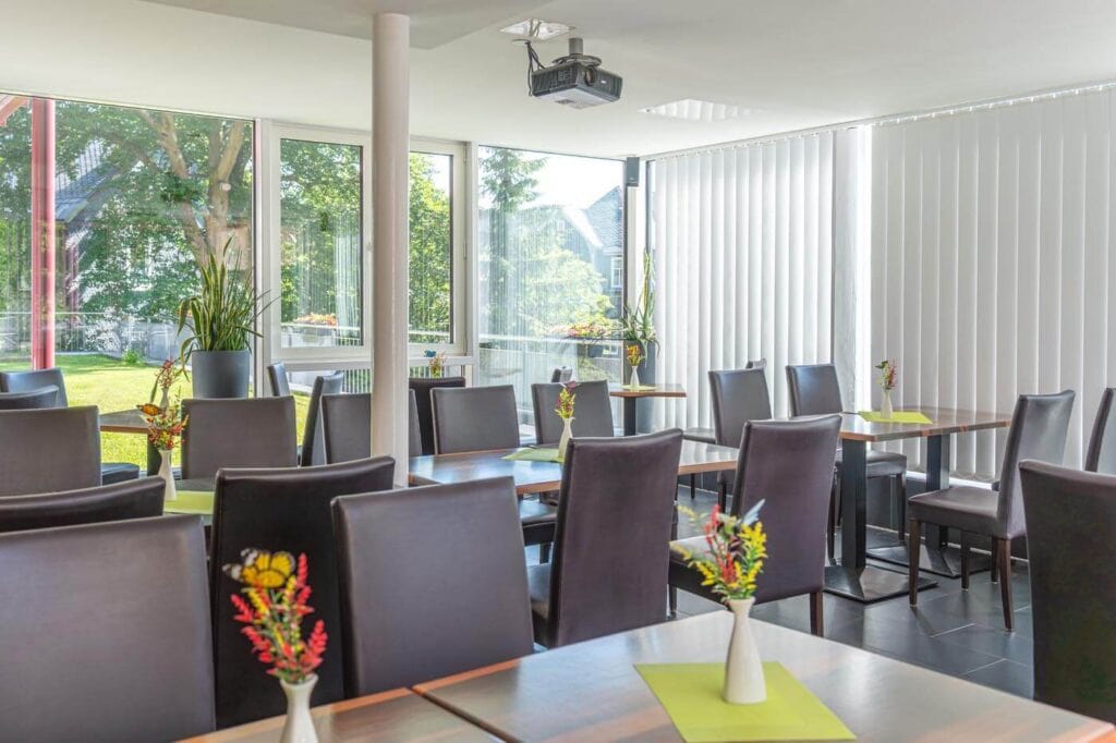 Aufenthaltsraum im Wintergarten mit modernen Tischen und Stühlen sowie Beamer