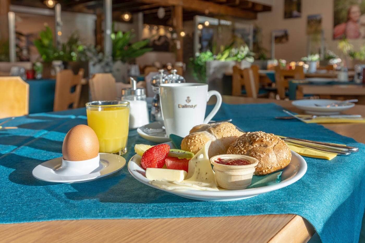 Frühstück im Hotel Oberhof Nahaufnahme eines Frühstücktischs mit Kaffee, Orangansaft, gekochtem Ei sowie einem Teller mit Brötchen, Marmelade, Käse und Obst.