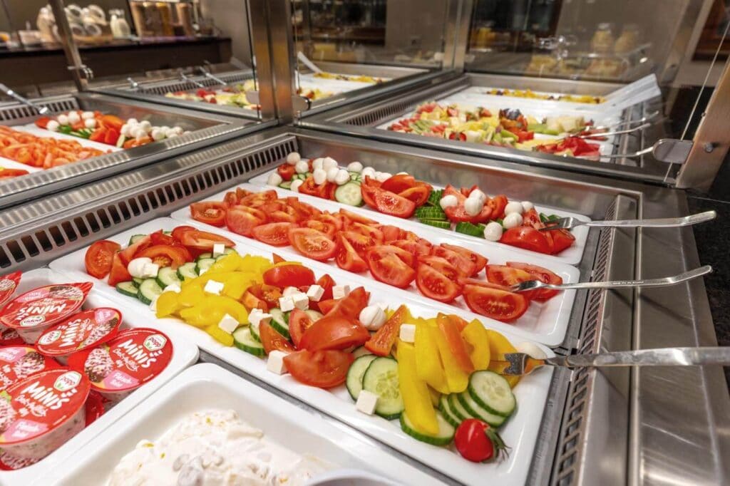 Frisches Gemüse liegt mit Feta und Mozzarella angerichtet auf dem Buffet, daneben befinden sich abgepackte Frühstücks-Aufstriche.